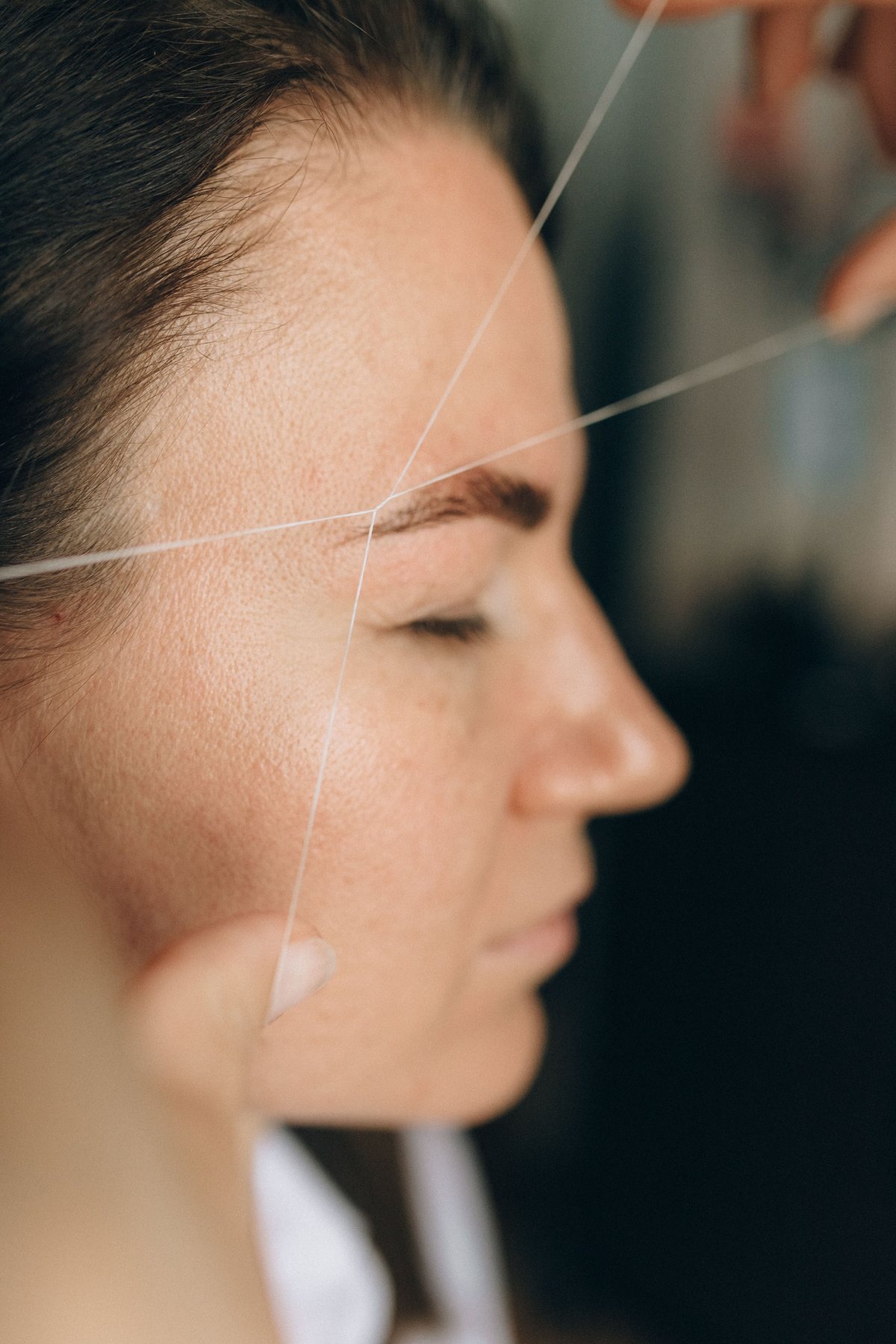 Side view of a woman receiving an eyebrow threading treatment; illustrative stock photograph