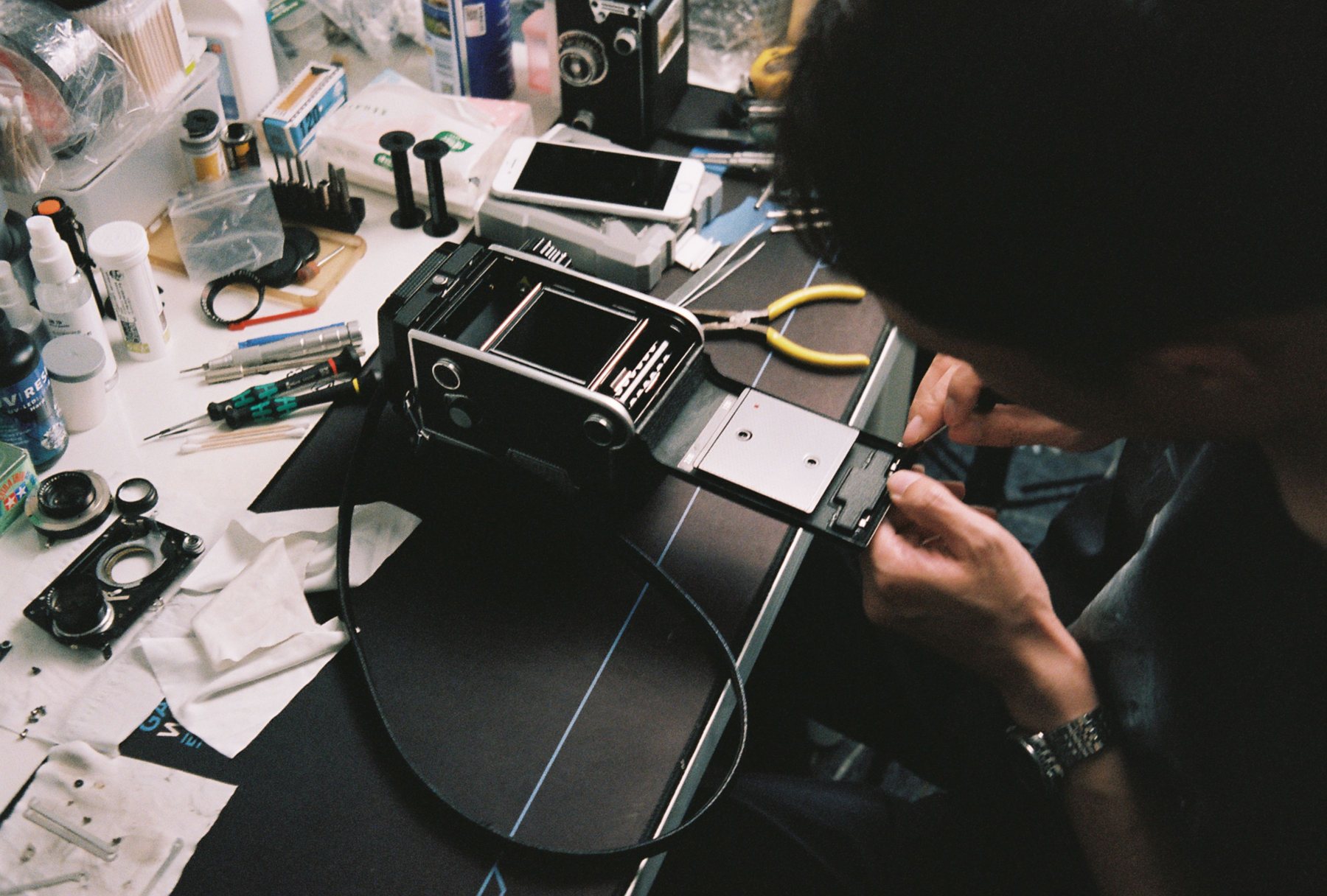 Hands repairing a vintage camera at a workbench with small tools; illustrative stock photograph